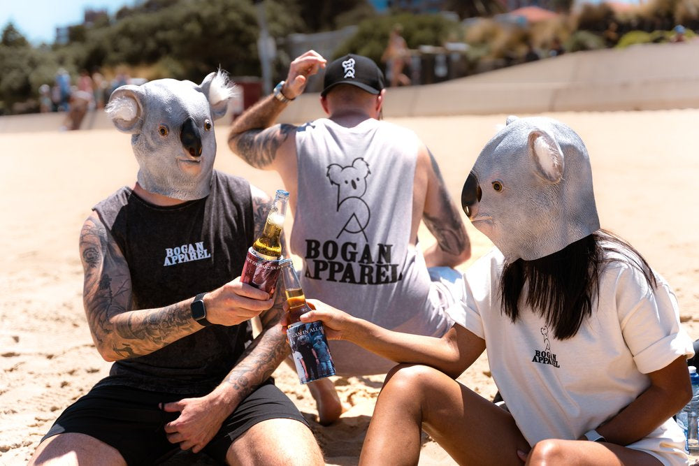 Group of people wearing koala masks on the beach, dressed in Bogan Apparel T-shirts and singlets, holding beers with branded stubby coolers.