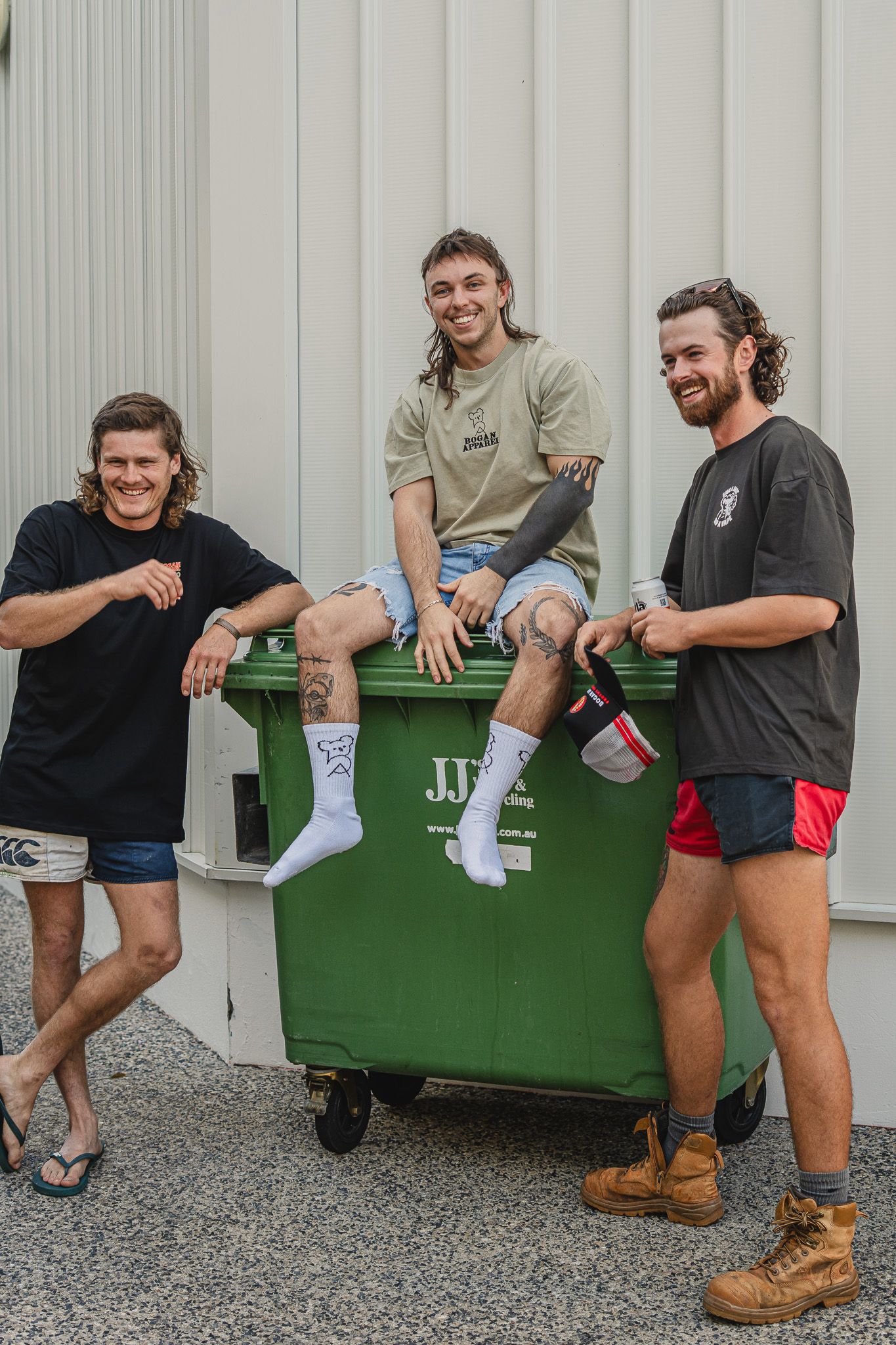 Three men posing around a green bin with visible Bogan Apparel branding.